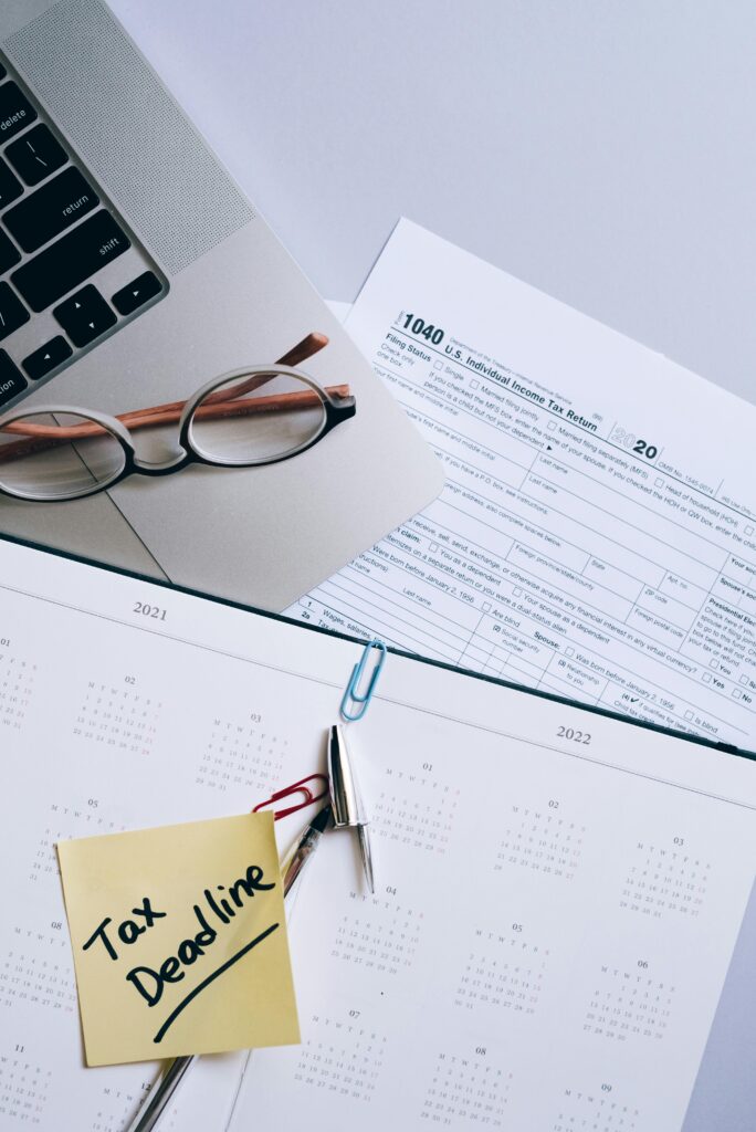 Overhead view of U.S. tax forms and financial documents on a green desk with eyeglasses and a calendar.